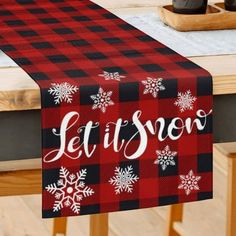 a red and black plaid table runner with let it snow written on the front in white