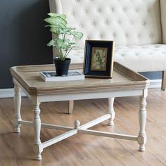 a white coffee table with a potted plant on top and a framed picture next to it