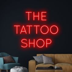 the tattoo shop neon sign is lit up against a dark wall with a couch and ottoman