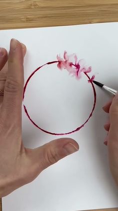 someone is doing something that looks like a circle with pink flowers on it and one hand holding a pencil