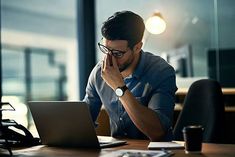 a man sitting in front of a laptop computer while holding his hand to his face