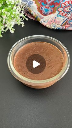 a glass bowl filled with brown liquid on top of a black table next to flowers