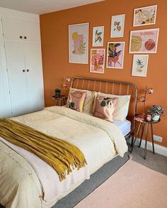 a bedroom with orange walls and pictures on the wall above the bed, along with two nightstands