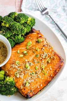 a white plate topped with broccoli and salmon next to a bowl of seasoning