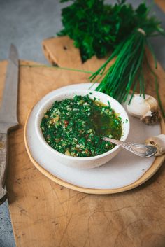 a white bowl filled with green food on top of a wooden cutting board