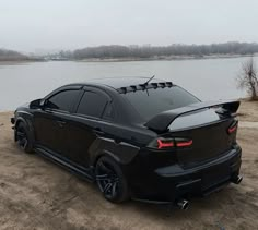 a black car parked on top of a sandy beach next to a body of water