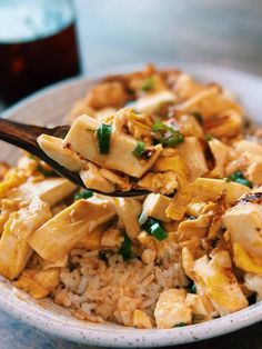 a white bowl filled with rice and chicken on top of a wooden table next to a drink