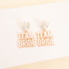 two pairs of earrings with the words team bride written in white and gold letters on them