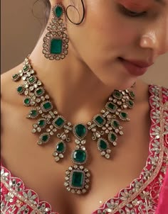 a woman wearing a necklace and earrings with green stones on it's collarline