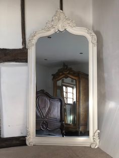 a large white mirror sitting on top of a wooden floor next to a dresser and chair