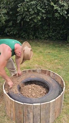 a man bending over to put something in a wooden barrel shaped fire pit on the grass