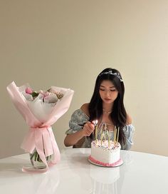 a woman sitting in front of a cake with candles on it next to a bouquet of flowers