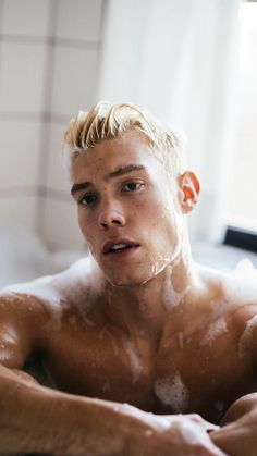 a shirtless man sitting in a bathtub with soap on his face and arms