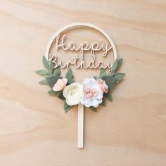 a cake topper that says happy birthday with flowers and leaves around it on a wooden surface