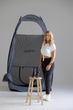 a woman standing in front of a tent with the door open and two stools next to it