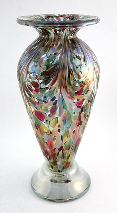 a colorful glass vase sitting on top of a metal stand in front of a white background