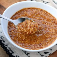 a white bowl filled with sauce on top of a wooden table next to a spoon