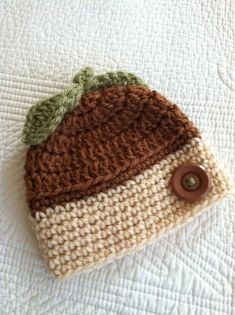 a crocheted hat is laying on top of a white bed with a brown button