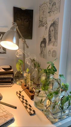 a desk with some plants on it next to a lamp and other office supplies in front of a window