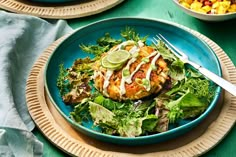 a blue plate topped with meat covered in sauce next to a bowl of salad and a fork