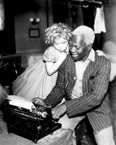 an old black and white photo of two people looking at something on a typewriter