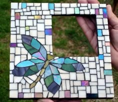 a hand holding up a small square shaped mosaic tile with a dragonfly on it