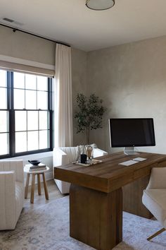 a desk with a computer on it in front of a window and two white chairs