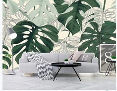 a living room with a couch, table and wallpaper that has monster leaves on it