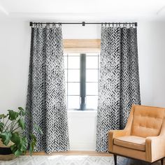 a living room with black and white curtains, a chair and potted plant in front of the window