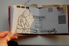 a person holding an open book with drawings on the pages and writing on paper attached to it