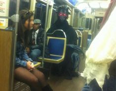 two people sitting on a subway train next to a black dog with glowing red eyes