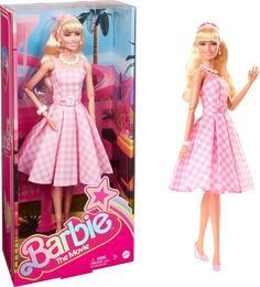 barbie doll in pink and white checkered dress next to cardboard box for barbie the movie