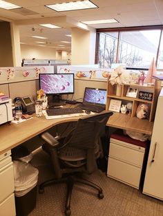 an office cubicle with two computer screens on the desk and several other items around it