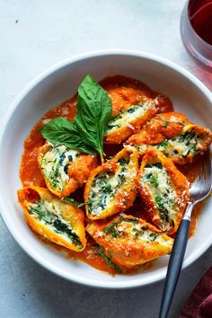 a white bowl filled with stuffed shells covered in sauce and garnished with basil