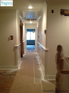 a woman in white dress walking down a hallway next to a doorway with curtains on both sides