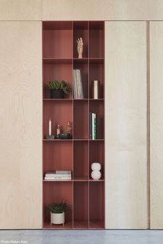 an open bookcase with books, plants and vases on it in front of a wooden wall