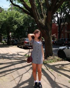 a woman standing on the sidewalk in front of a tree with her hands behind her head