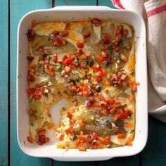 a casserole dish with vegetables in it on a blue wooden table next to a napkin