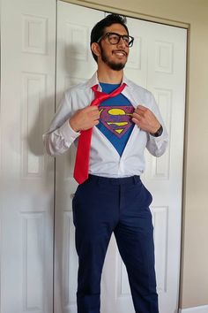 a man wearing a superman shirt and tie standing in front of a door with his hands on his hips