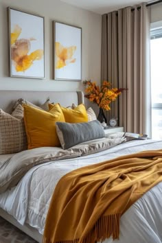 a bed with yellow and gray pillows on top of it next to two framed pictures