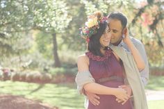 a pregnant woman is hugging her husband while he talks on his cell phone in the park