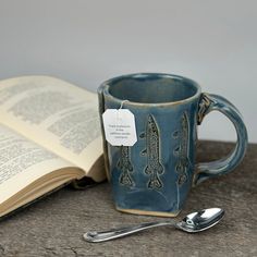 an open book next to a coffee cup and spoon with a tag on the handle