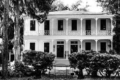 an old white house with trees and bushes around it