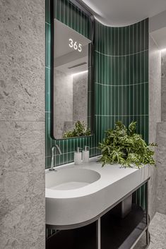 a green tiled bathroom with a sink and mirror in it's corner, surrounded by greenery