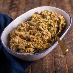 a white bowl filled with stuffing on top of a wooden table next to a blue napkin