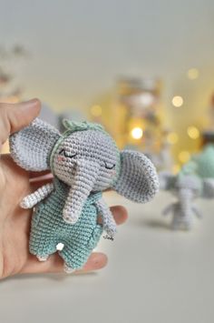 a small crocheted elephant is being held up by someone's hand with other tiny elephants in the background