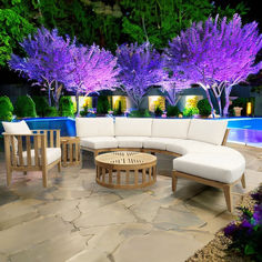 an outdoor living area with white furniture and purple trees in the background at night time