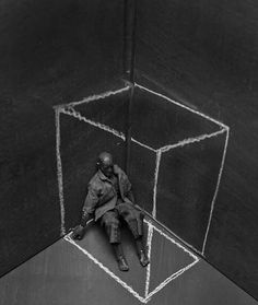 a black and white photo of a man sitting in front of a cube