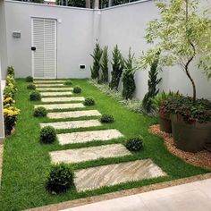 a small garden with stepping stones and plants in the grass, next to a white building