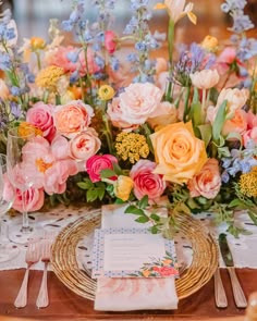 the table is set with pink, yellow and blue flowers on it's place setting